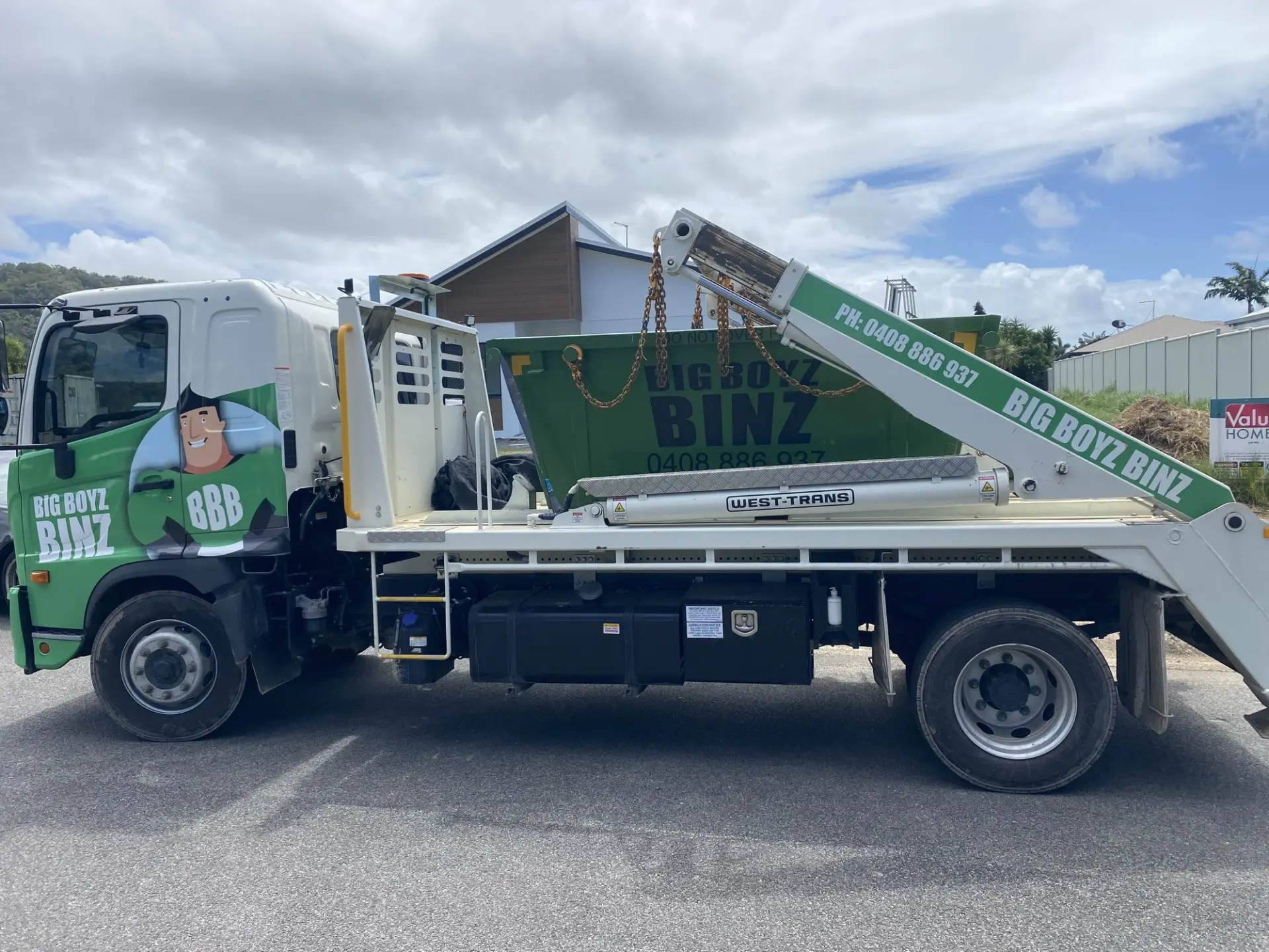 Big Boyz Binz truck with a loaded green skip bin on its tray outside a Cairns building site