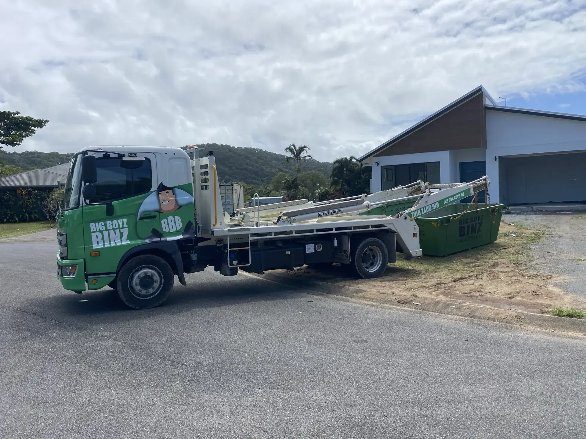 Big Boyz Binz truck lowering a green skip bin onto a driveway in Cairns