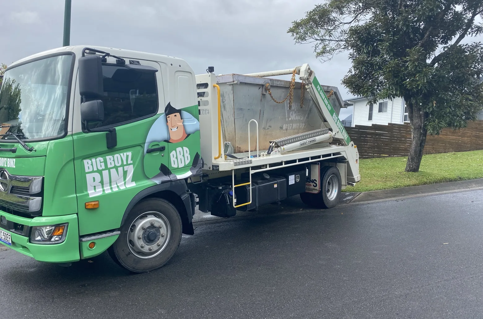 Big Boyz Binz truck carrying a bare steel skip bin on its arms down a Cairns street