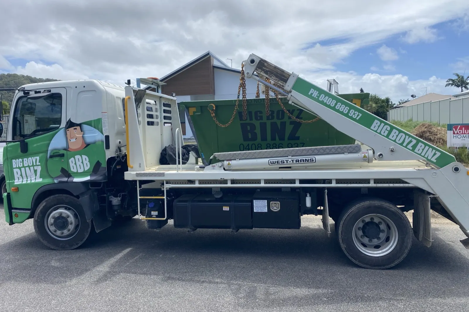 Big Boyz Binz truck with a loaded green skip bin on its tray outside a Cairns building site