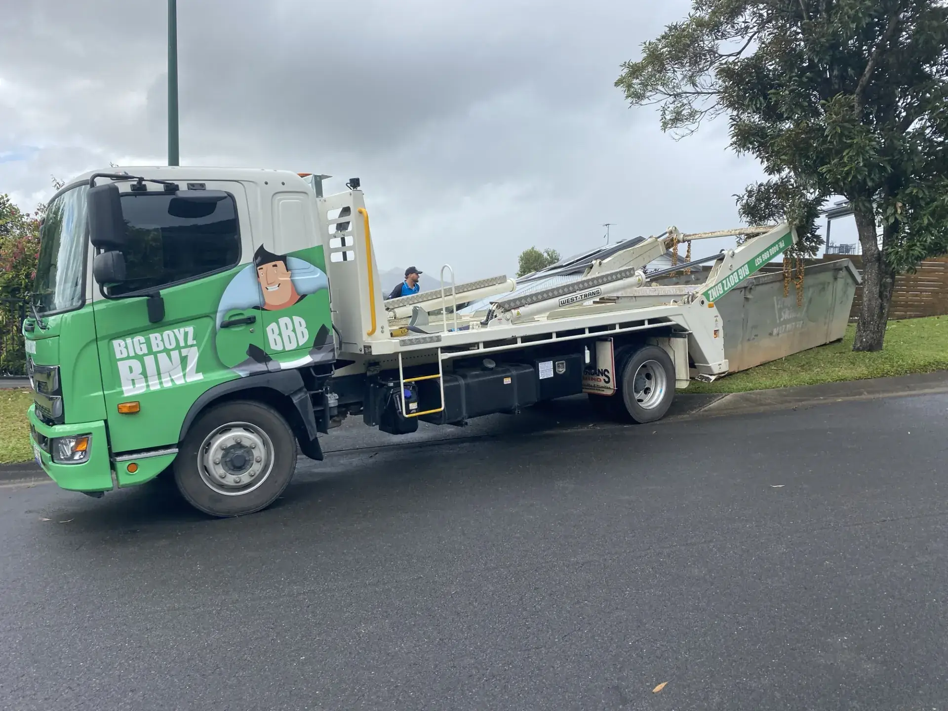Big Boyz Binz truck setting a skip bin down on a lawn beside a fence in Cairns
