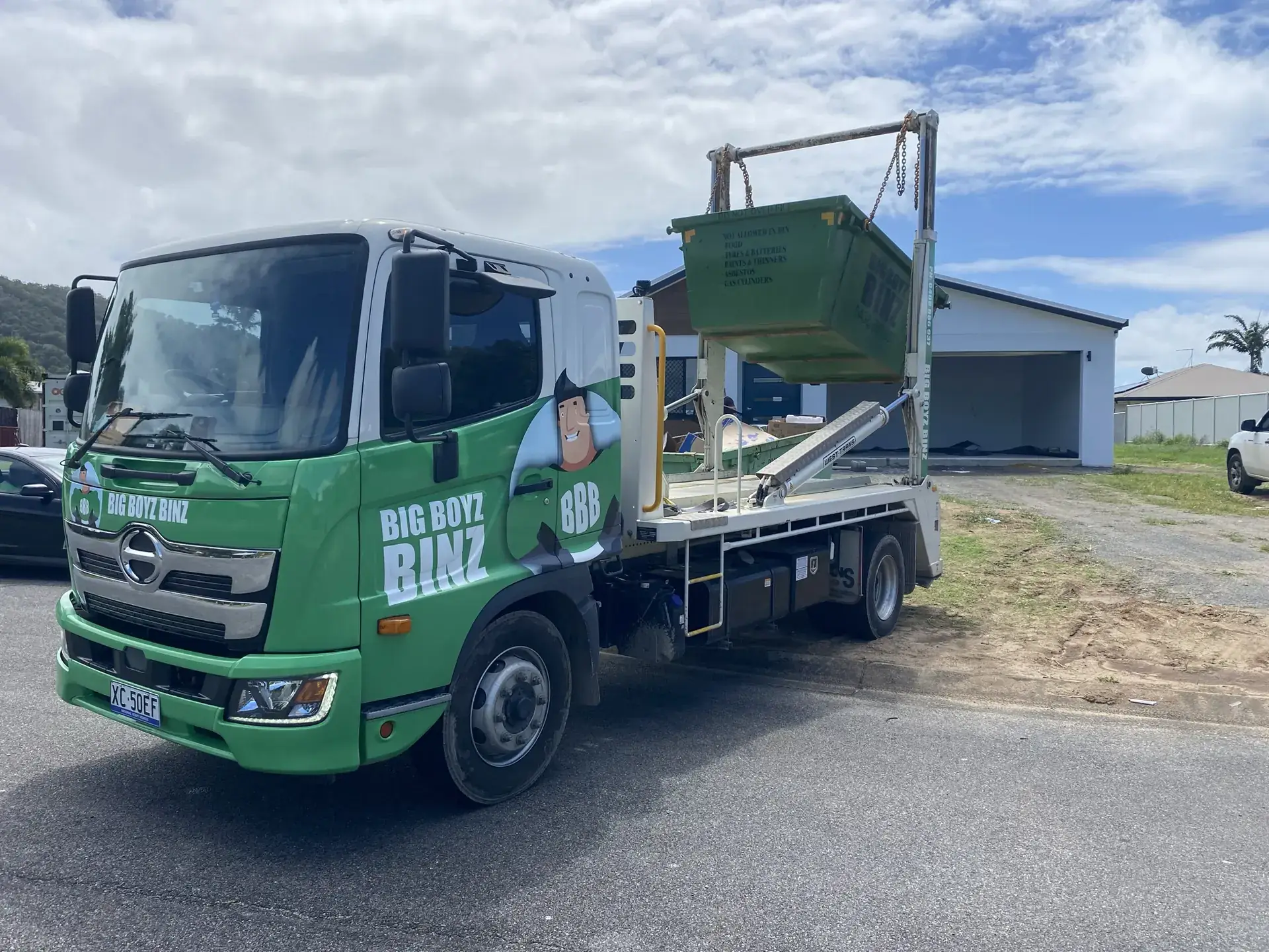 Big Boyz Binz truck lifting a green skip bin onto its arms on a Cairns street